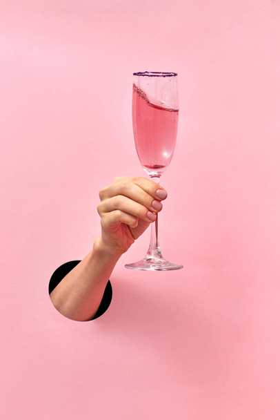 Woman hand from the hole holds glass with rose wine on a pastel pink background, copy space. Holiday concept. - Foto, Imagem