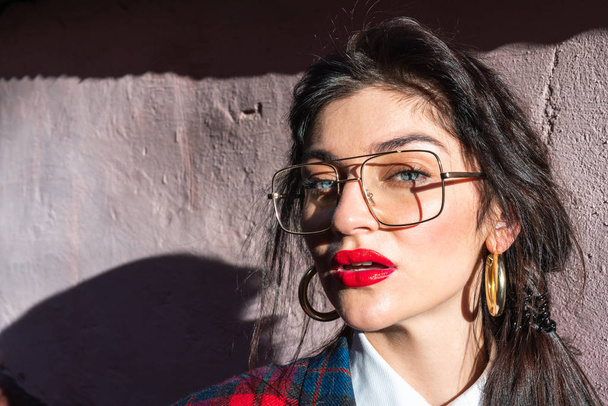 Close up portrait of the beautiful gorgeous young lady in glasses with brunette hair and red lips, sun rays fall on her face - Photo, Image