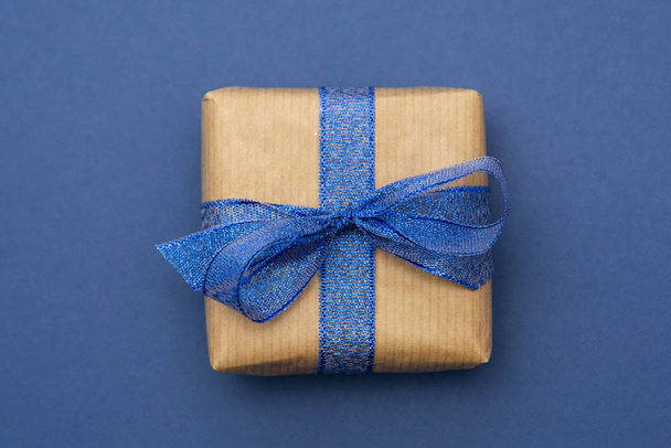 Craft paper wrapped gift box isolated on blue background, flat lay. Abstract Christmas gift. - Foto, immagini
