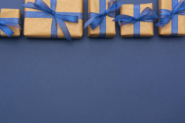 Craft paper wrapped gift boxes in a row on blue background, flat lay with copy space. Christmas abstract mock up. - Photo, Image