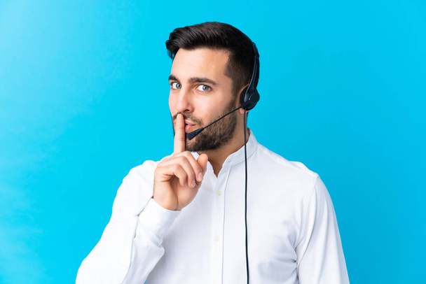 Uomo telemarketer che lavora con un auricolare su sfondo blu isolato facendo gesto di silenzio
 - Foto, immagini