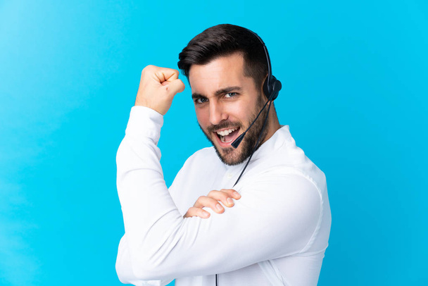 Hombre de telemarketer trabajando con un auricular sobre fondo azul aislado haciendo un gesto fuerte
 - Foto, imagen