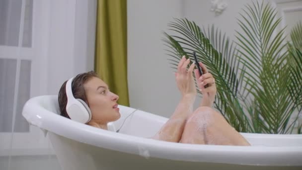 Hermosa mujer escuchando música en la bañera disfrutando de relajante estilo de vida baño de burbujas cuidado del cuerpo natural real
. - Imágenes, Vídeo