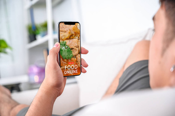 мужчина держит в руке телефон с экраном доставки еды на столе в
  - Фото, изображение