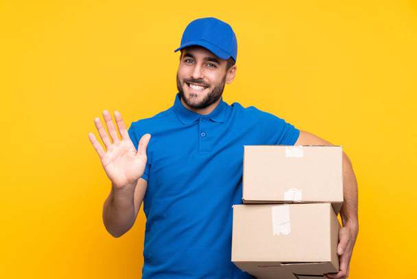 Delivery man over isolated yellow background saluting with hand with happy expression - Photo, Image
