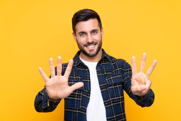 Homem bonito jovem com barba sobre fundo amarelo isolado contando oito com dedos
 - Foto, Imagem