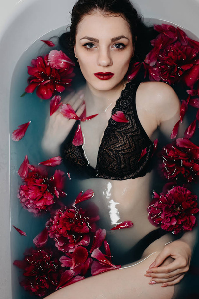 girl with makeup in bra lies and enjoys in bath with peonies - Photo, image