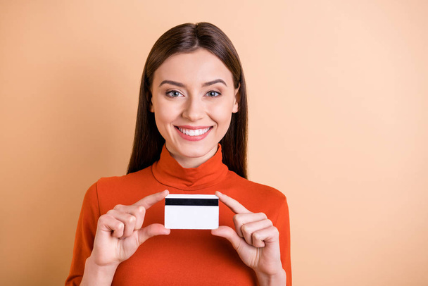 Photo of charming beautiful girlfriend presenting her credit hard holding it with hands smiling toothily wearing red turtleneck isolated beige pastel color background - Foto, Bild