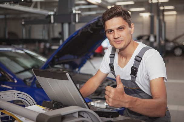 młody przystojny mechanik samochodowy naprawy pojazdu w jego garażu - Zdjęcie, obraz