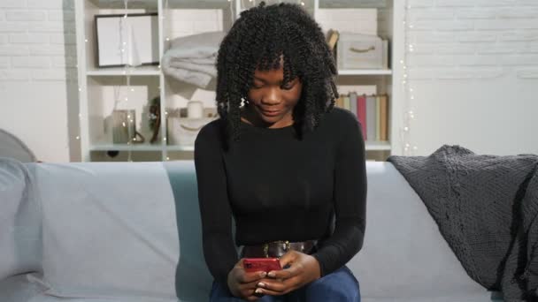 African American lady with curly hair types on smartphone - Footage, Video