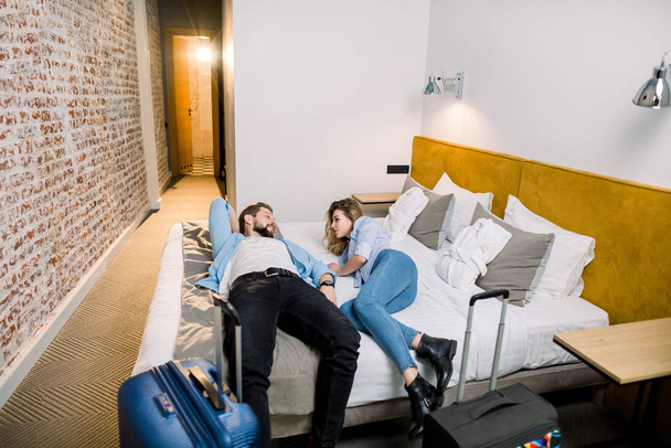 Couple of tourists with big suitcases relaxing after trip lying on the bed in an hotel room on vacations - Fotografie, Obrázek