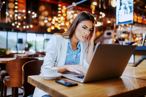 Привлекательная нервная кавказская деловая женщина, сидящая в кафе и пользующаяся ноутбуком. Она только что прочитала письмо от своего босса.
. - Фото, изображение