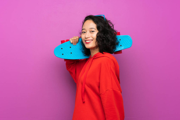 Asian młody dziewczyna z skate na fioletowy tło - Zdjęcie, obraz