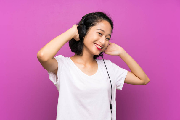 Aasian nuori tyttö kuuntelee musiikkia mobiili yli eristetty violetti seinä
 - Valokuva, kuva