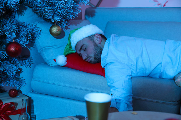 Drunk man wearing Santa hat sleeping on sofa after New Year party - 写真・画像