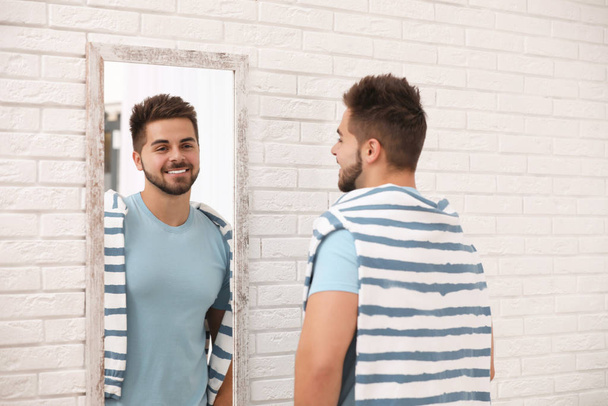 Młody człowiek spogląda na siebie w dużym lustrze w domu - Zdjęcie, obraz