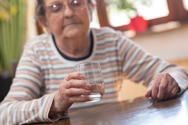 Mulher idosa segurando um copo de água
 - Foto, Imagem