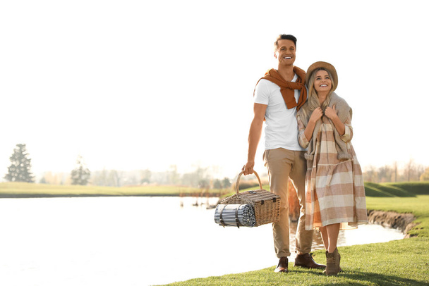 Young couple with picnic basket near lake on sunny day - Photo, Image