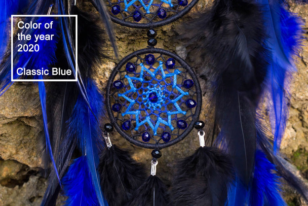 Мечтатель ручной работы с нитками из перьев и веревкой из бусин, висящей в классическом синем модном цвете 2020 года
. - Фото, изображение