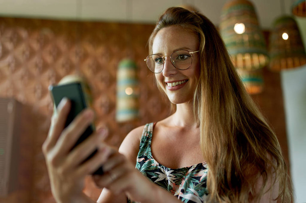 Beautiful millennial woman with glasses using smartphone for vid - 写真・画像