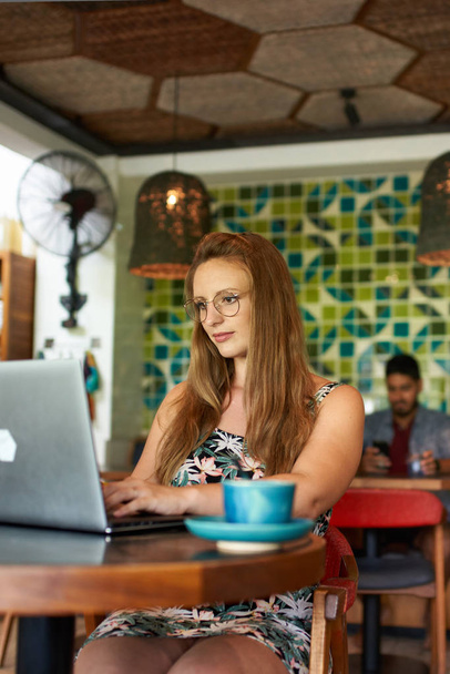 Beautiful millennial woman typing on laptop sitting at table in - Photo, Image