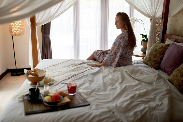 Calme belle femme avec peignoir assis dans une chambre d'hôtel lumineuse
 - Photo, image