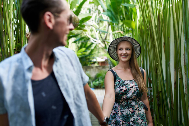 Young happy hipster couple holding hands in tropical plant passa - 写真・画像