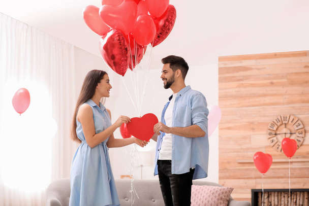 Lovely couple with heart shaped balloons in living room. Valentine's day celebration - Φωτογραφία, εικόνα
