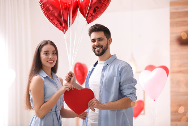 Lovely couple with heart shaped balloons in living room. Valentine's day celebration - Fotografie, Obrázek