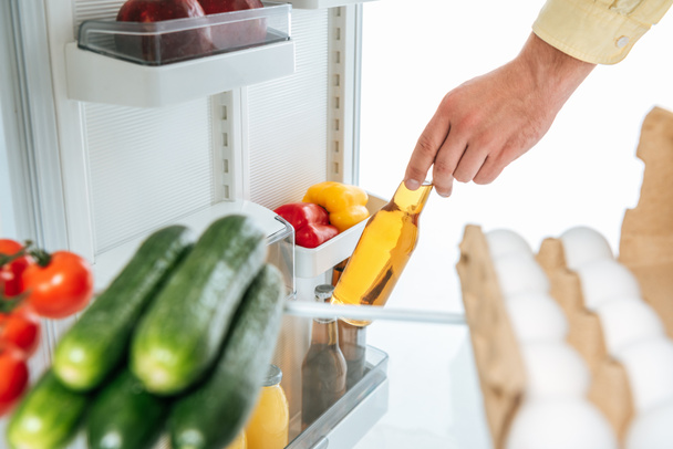 cropped view of man taking bottle of beer out from fridge with fresh food on shelves isolated on white - Photo, Image
