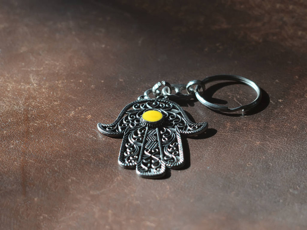 A key ring in the form of Fatima Hand on a brown leather background. Ancient symbol and traditional modern tourist souvenir of Tunisia - Photo, Image
