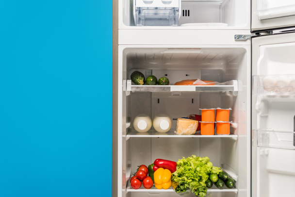 open fridge full of fresh food on shelves isolated on blue - Foto, afbeelding
