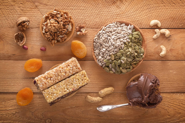 Bars of sports nutrition from nuts, seeds and chocolate paste - vegetable natural protein, a mixture of dried fruits, assorted nuts and seeds on a wooden table. Top view - Photo, Image