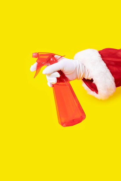 Kerstman handschoen hand gele achtergrond spray dispenser een rood pak kopieerruimte - Foto, afbeelding
