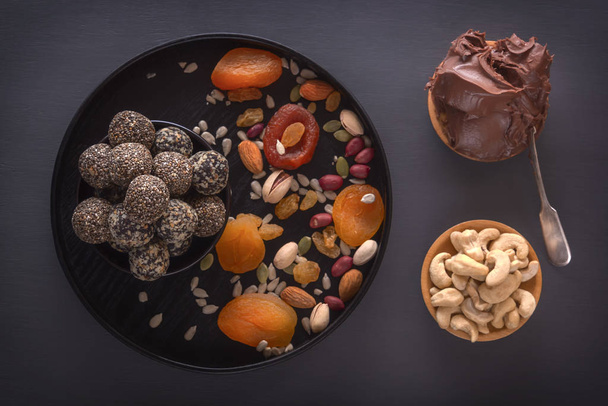 Mordidas de energia crua saudáveis naturais, pasta de chocolate e mistura de frutas secas com nozes em uma mesa escura. Vista superior
 - Foto, Imagem