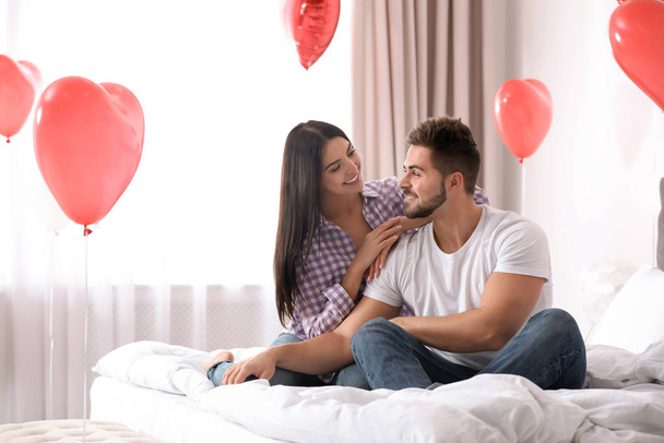 Lovely young couple in bedroom decorated with heart shaped balloons. Valentine's day celebration - Zdjęcie, obraz