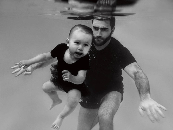 水泳プールで水中に潜るように娘に教えるハンサムな陽気な父親。家族、レッスン、休日の概念.  - 写真・画像