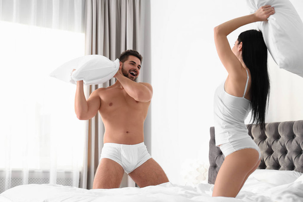 junges Paar in weißer Unterwäsche bei Kissenschlacht im heimischen Bett - Foto, Bild