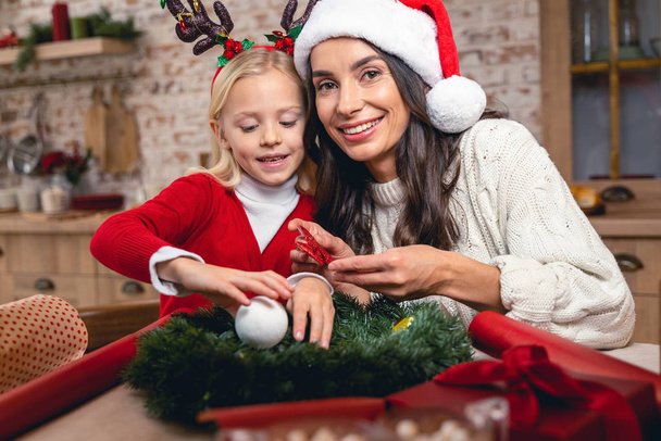 Smiling mother holding a Christmas wreath bow - Zdjęcie, obraz
