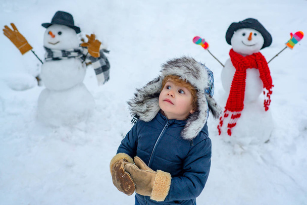 Snowman and funny child the friend is standing in winter hat and scarf with red nose. Merry Christmas and Happy new year. Christmas winter children. - Фото, изображение