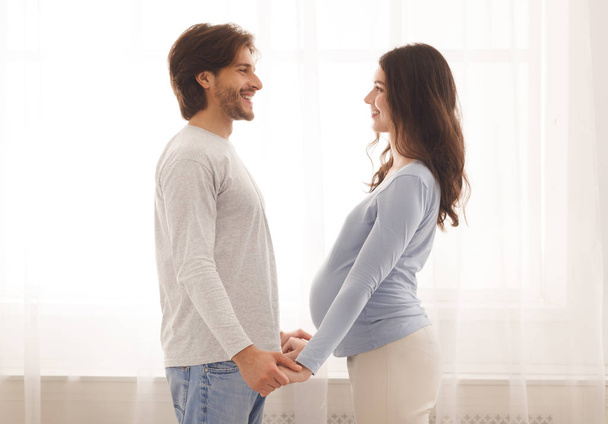 Embarazada pareja sosteniendo las manos y mirando el uno al otro con amor
 - Foto, imagen