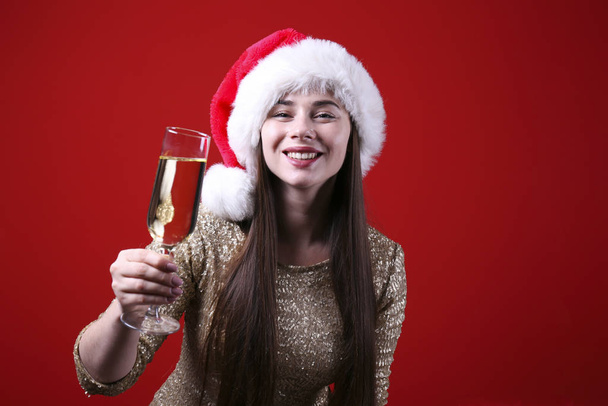 Smiling woman wearing santa hat on red wall background. - Фото, изображение