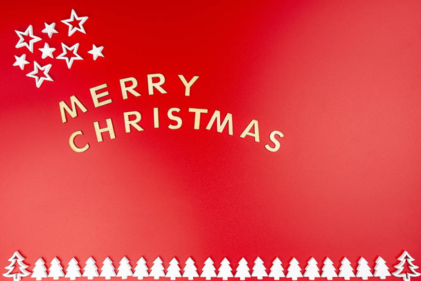 Ahşap harflerden yapılmış Mutlu Noeller yazılıydı. Yukardan düz yatıyordu. Kırmızı arka planda izole edilmişti. Beyaz ahşap Noel ağaçları en altta sıralanmış. x1 - Fotoğraf, Görsel