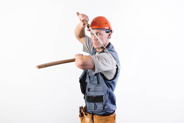 O construtor mostra uma luta com uma katana. Reparador vestindo um capacete e roupas de trabalho
. - Foto, Imagem