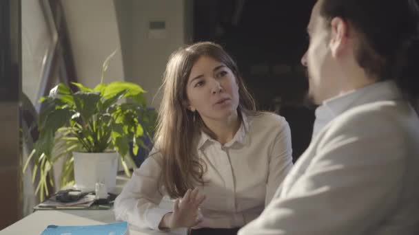 Close-up of young Caucasian businesswoman sitting with male colleague in the office at night and talking. Beautiful female office worker discussing business issues with coworker. Management, teamwork. - Filmagem, Vídeo