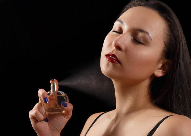 A portrait of a beautiful woman spraying perfume. on black - Fotografie, Obrázek