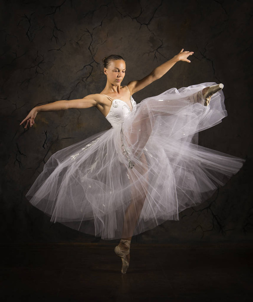 Slender girl in a white corset tutu dancing ballet. Studio shooting on a dark background, isolated images. - Photo, image