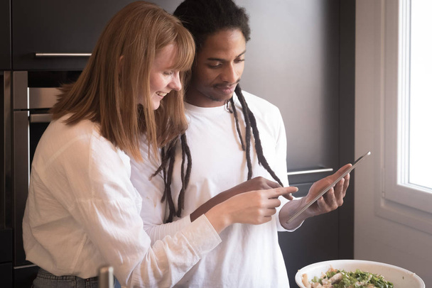 Wielokulturowa para patrząca na tablet w kuchni - Zdjęcie, obraz