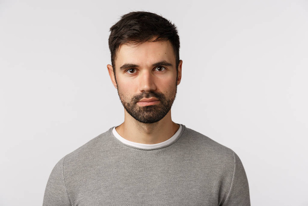 Close-up shot serious and determined handsome, adult masculine bearded man in grey sweater, looking with casual expression camera, standing still, awaiting important news, white background - Foto, immagini