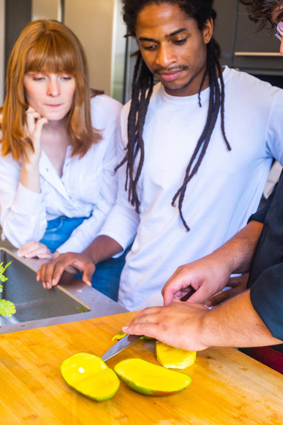Cozinhe cortando uma manga em pedaços com uma faca na frente de um casal
 - Foto, Imagem